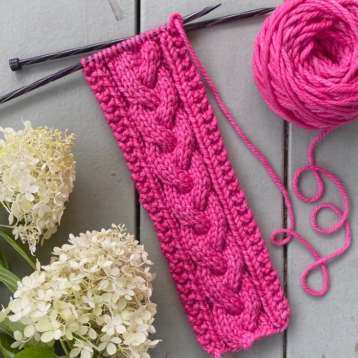 a pink knitted headband next to flowers and yarn