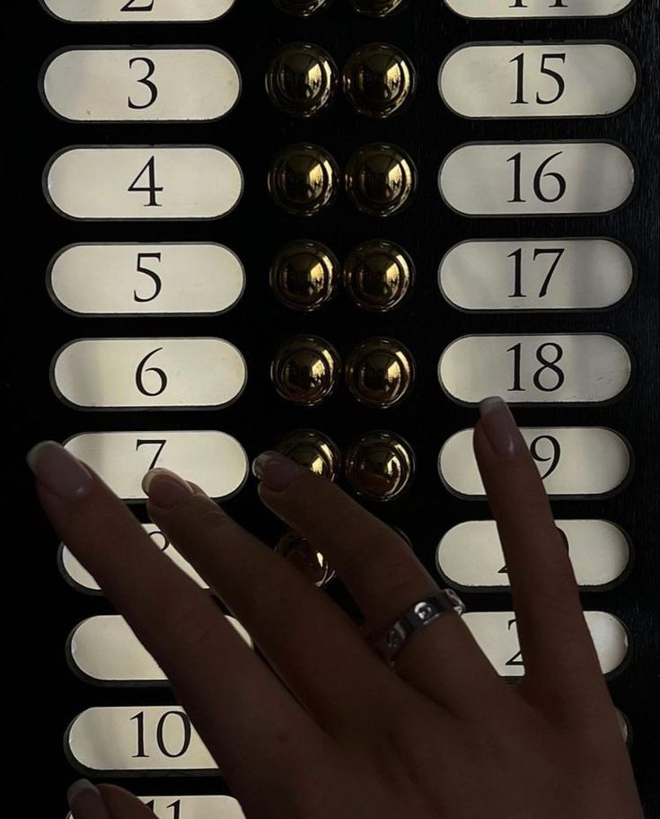 a woman's hand is touching the numbers on an elevator button board with her fingers