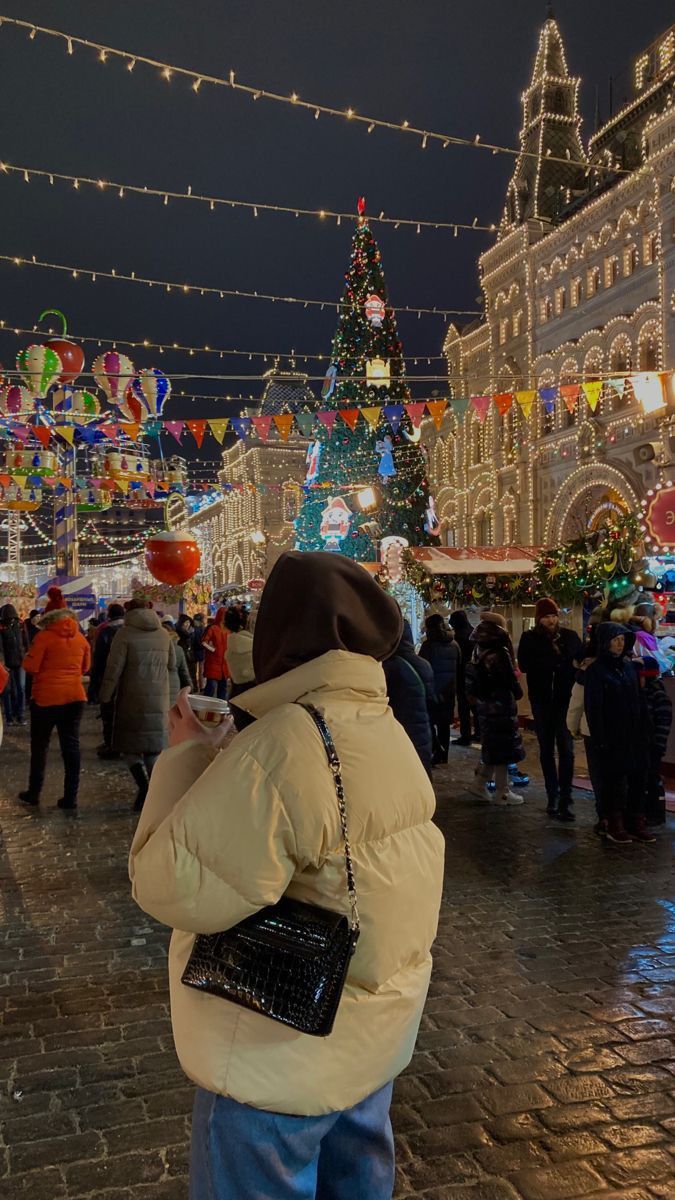 a woman standing in the middle of a street with christmas lights strung all around her