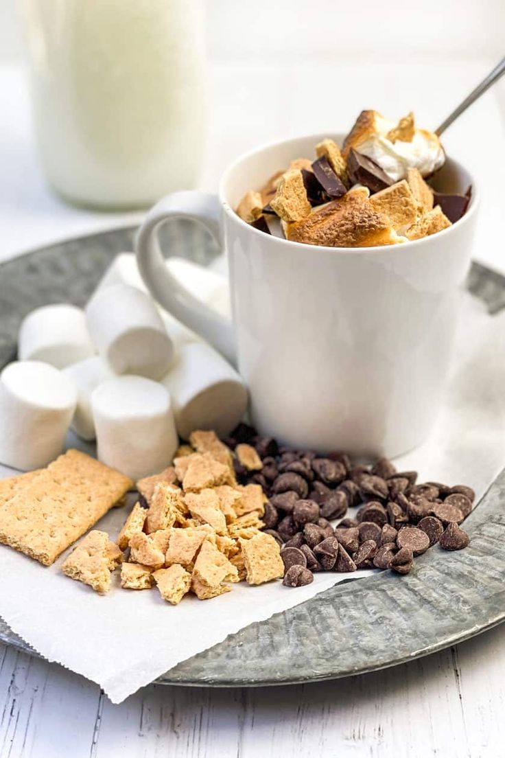 a cup filled with marshmallows, chocolate chips and graham crackers on a plate