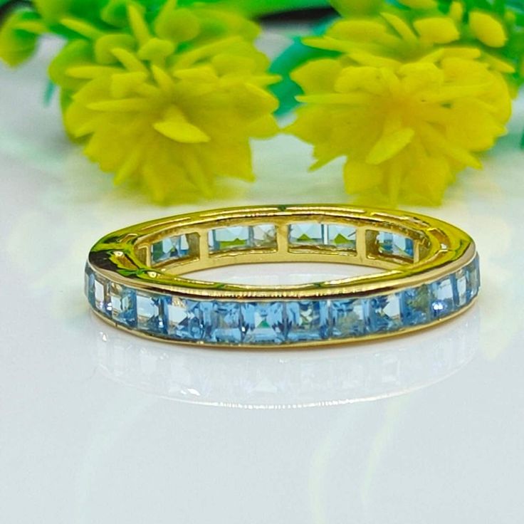 a yellow gold ring with blue topaz stones on it and flowers in the background