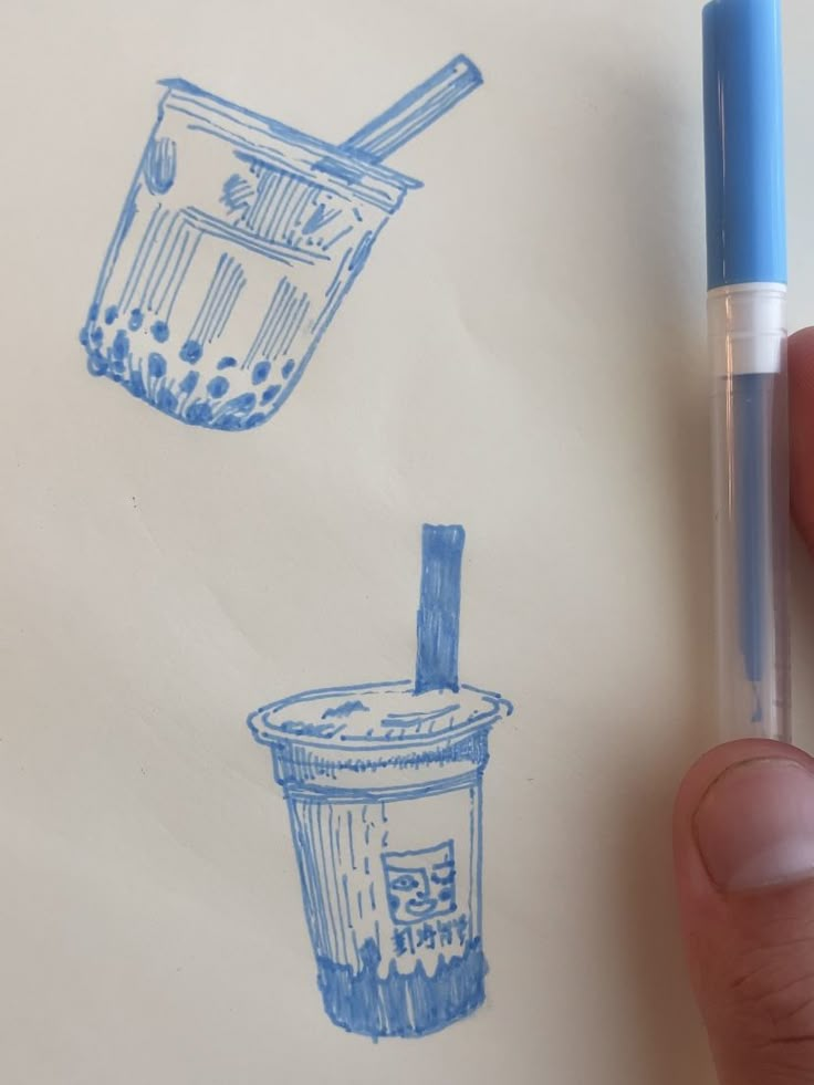 a hand is holding a pen and drawing two cups with straws on paper,