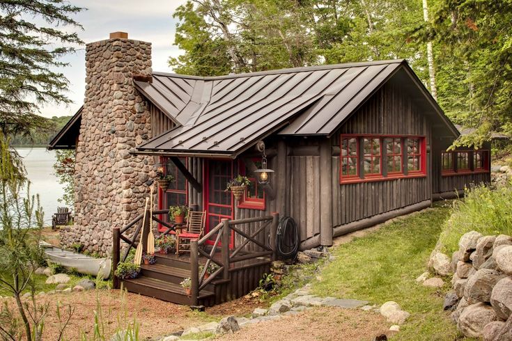 a small cabin sits on the shore of a lake in front of a stone chimney