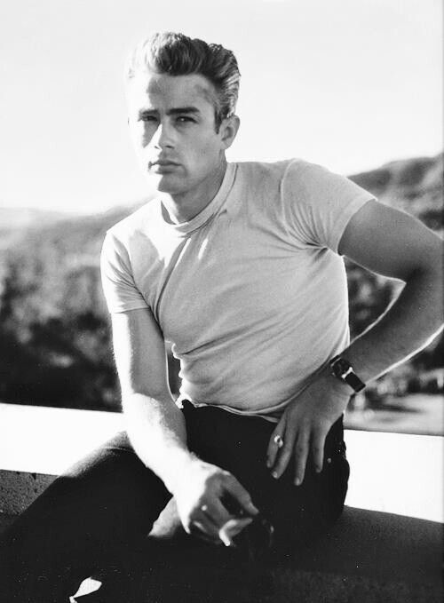 a black and white photo of a man sitting on a ledge with his hands on his hips