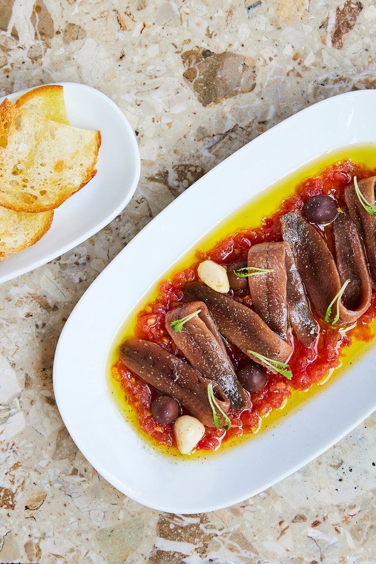 a white plate topped with meat covered in sauce next to two slices of bread on top of a table