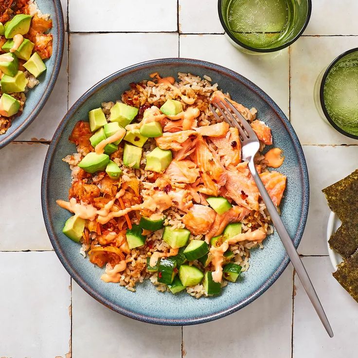 two bowls filled with rice and vegetables on top of a white tile floor next to drinks