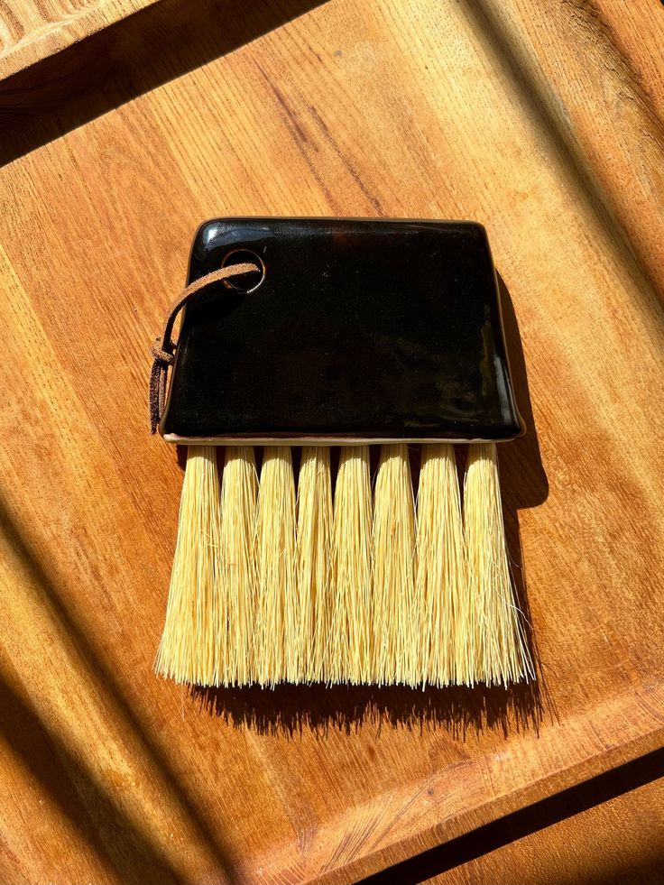 a brush sitting on top of a wooden table next to a black container filled with yellow hair