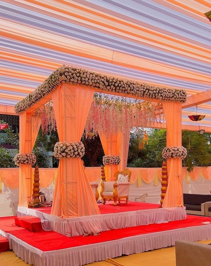 an outdoor wedding setup with pink and white draping on the ceiling, decorated with flowers