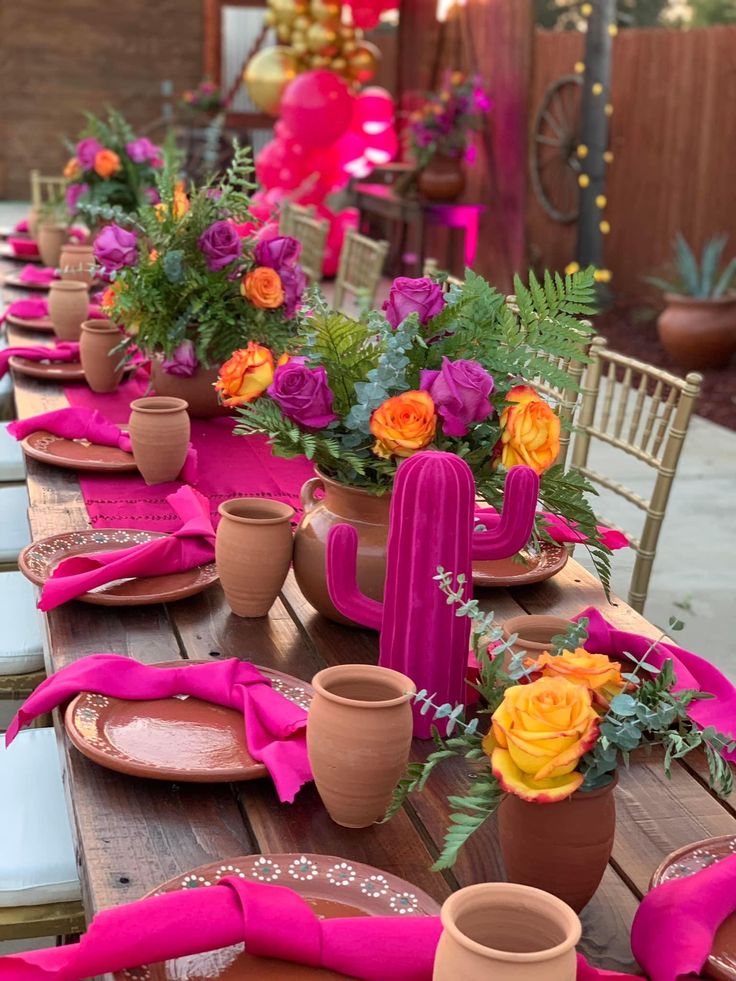 the table is set with pink napkins and potted plants on top of it