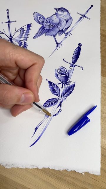 a person is drawing with blue ink on white paper and holding a pen in their left hand