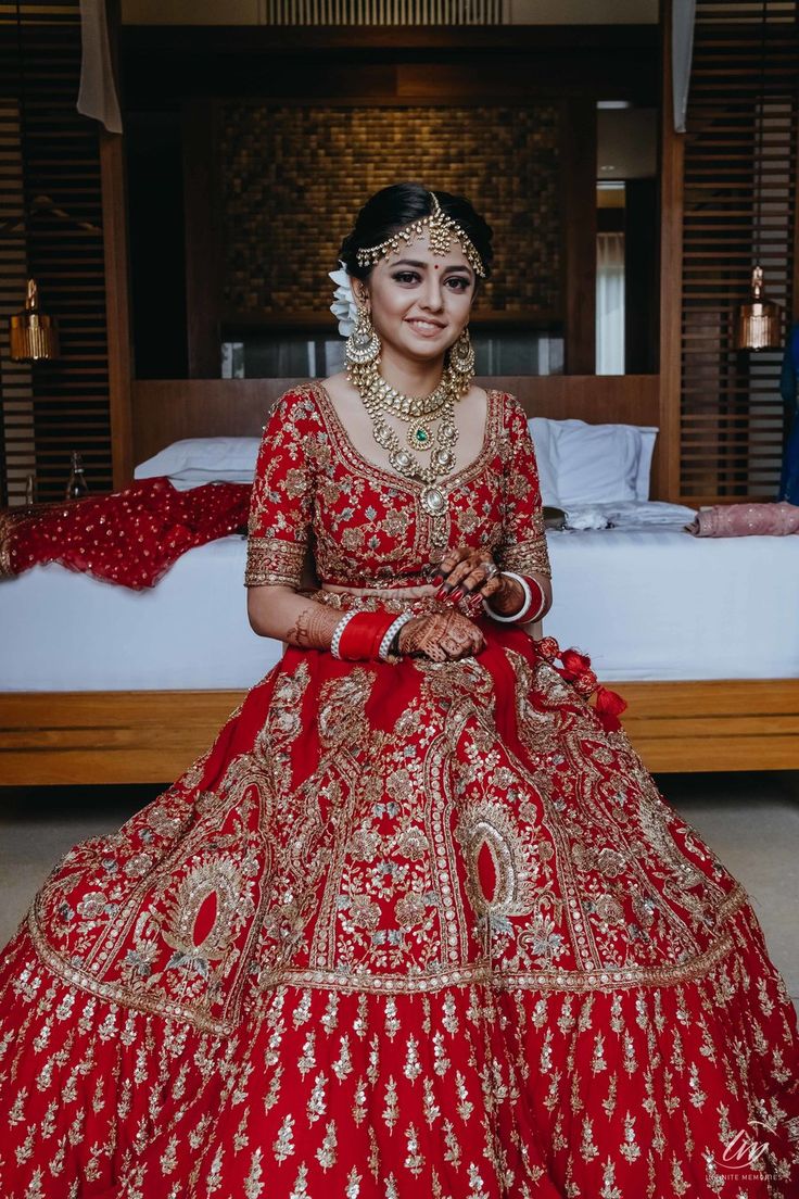 a woman in a red and gold bridal gown sitting on the floor next to a bed