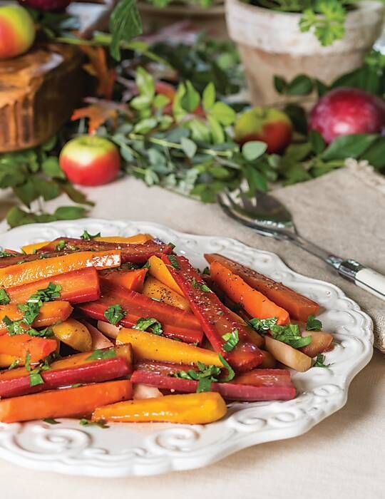 a white plate topped with carrots and parsley on top of a table next to apples