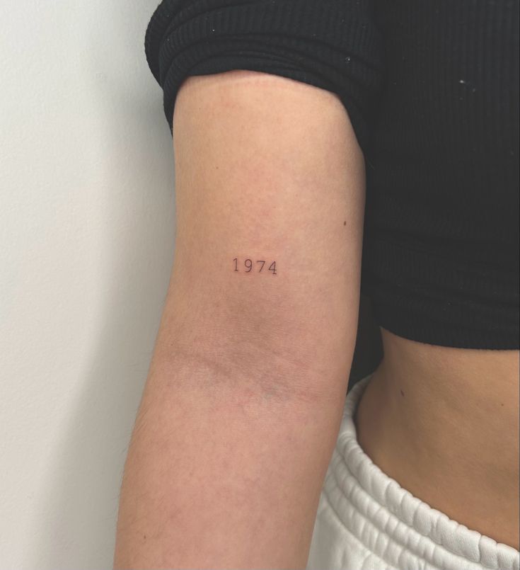 a woman with a small tattoo on her arm and the word 1974 written in cursive font