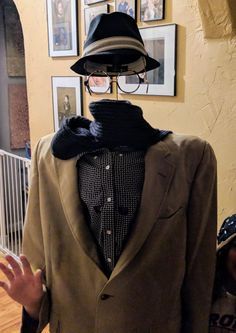 a mannequin wearing a suit and hat in front of pictures on the wall