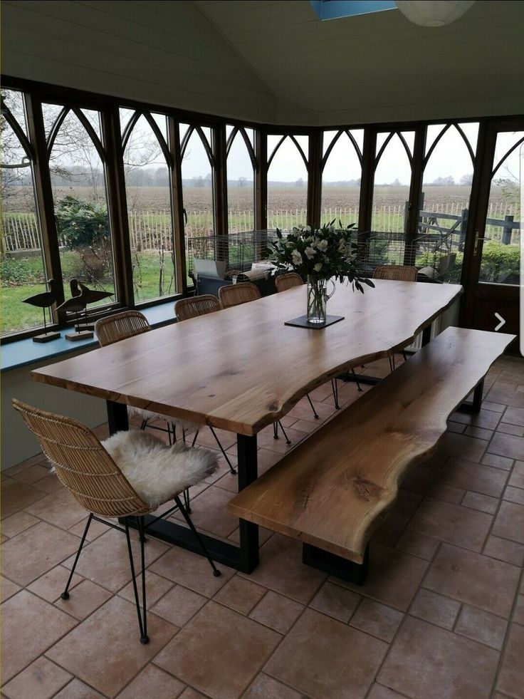 a large wooden table sitting under a window next to a vase with flowers on it