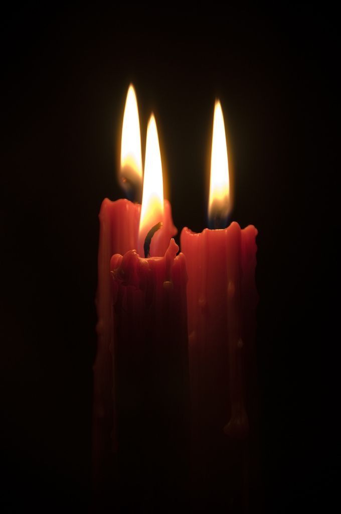 three lit candles in the dark with one candle on each side and two are red