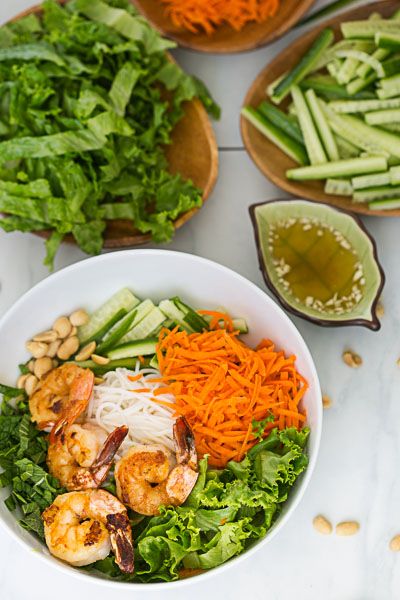 a white bowl filled with shrimp, carrots and lettuce on top of a table