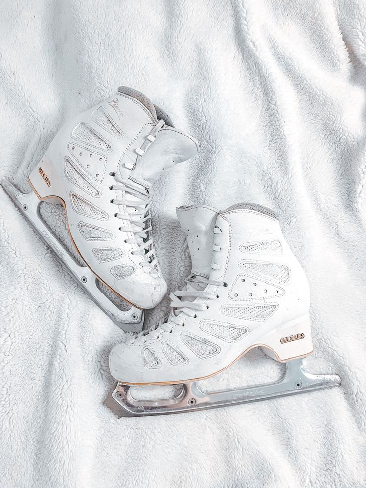 pair of white ice skates sitting on top of a bed next to each other