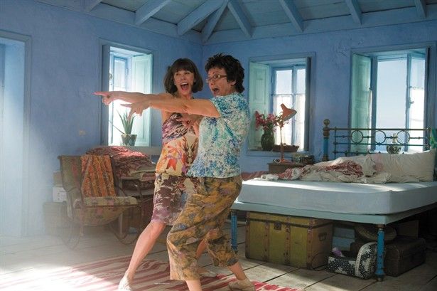 two people are dancing in a room with blue walls and flooring, one is pointing at the other