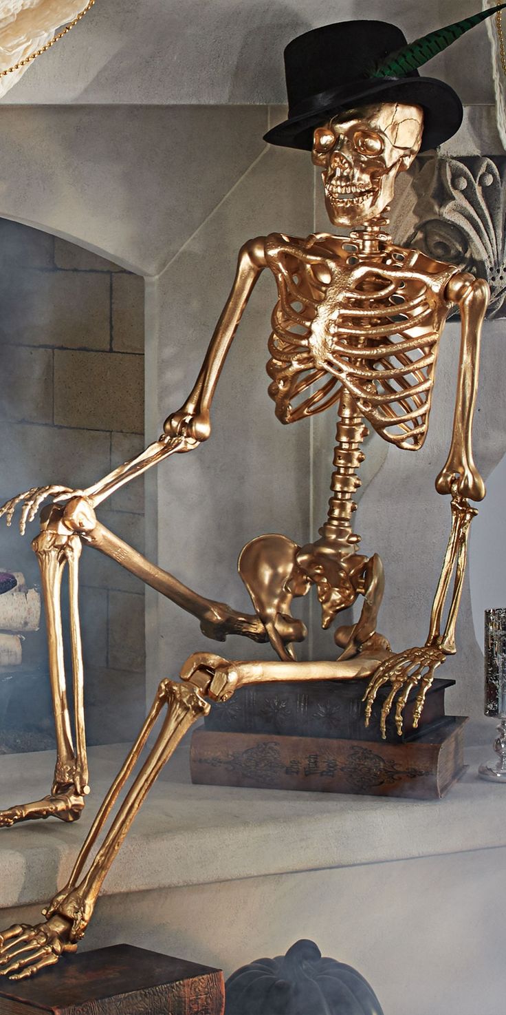 a golden skeleton sitting on top of a wooden table next to a black hat and other items