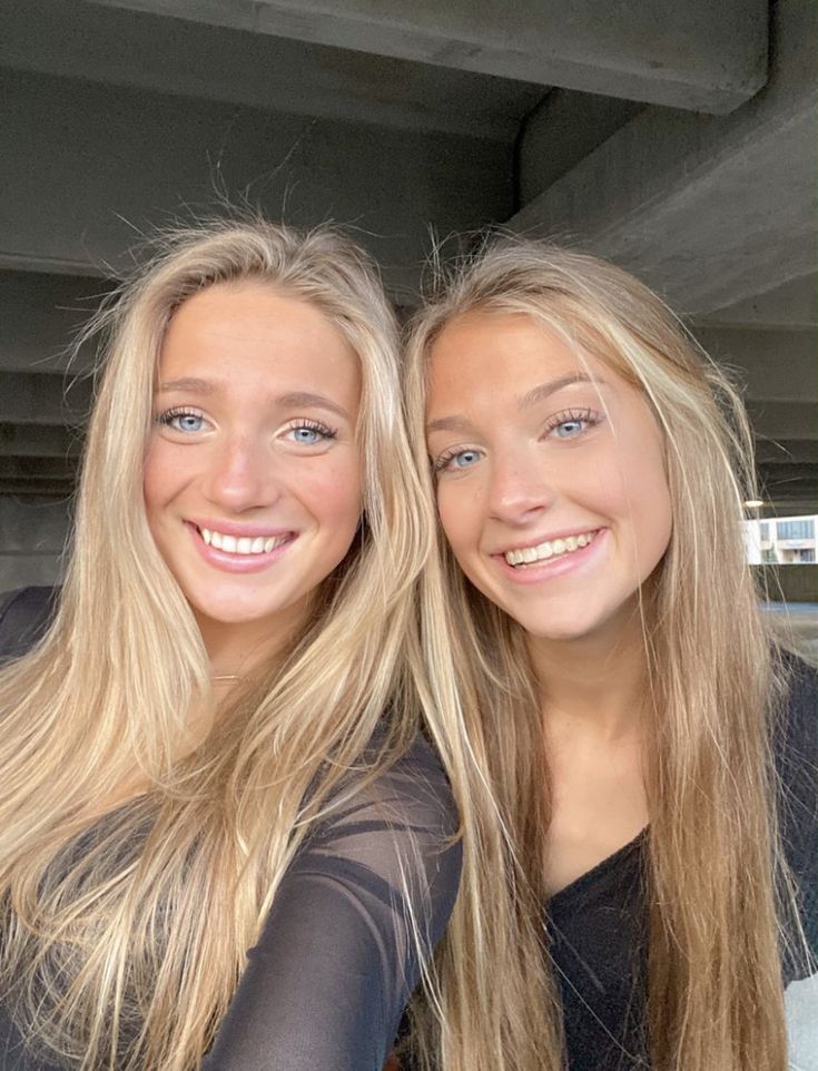 two beautiful young women sitting next to each other in front of a building and smiling at the camera