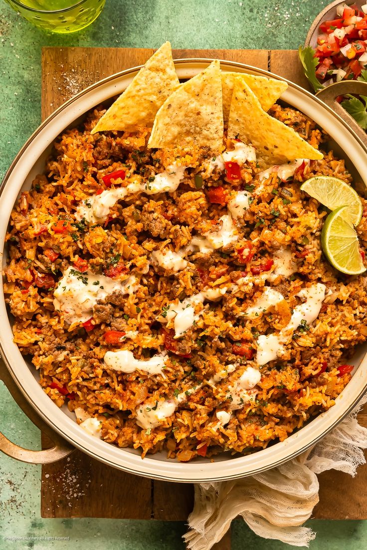 mexican food in a bowl with tortilla chips and limes on the side