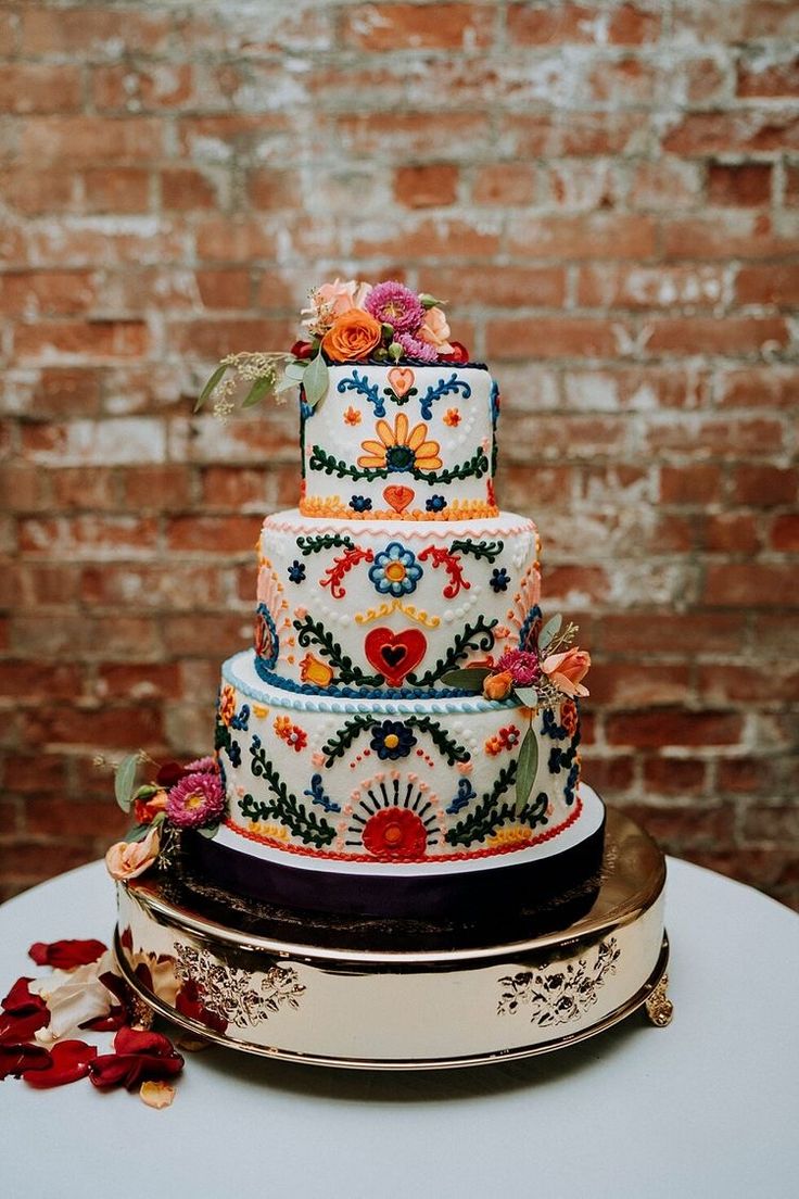 a multi - tiered wedding cake with flowers on top sits on a table in front of a brick wall