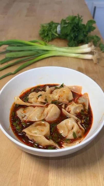 a white bowl filled with dumplings on top of a wooden table next to celery