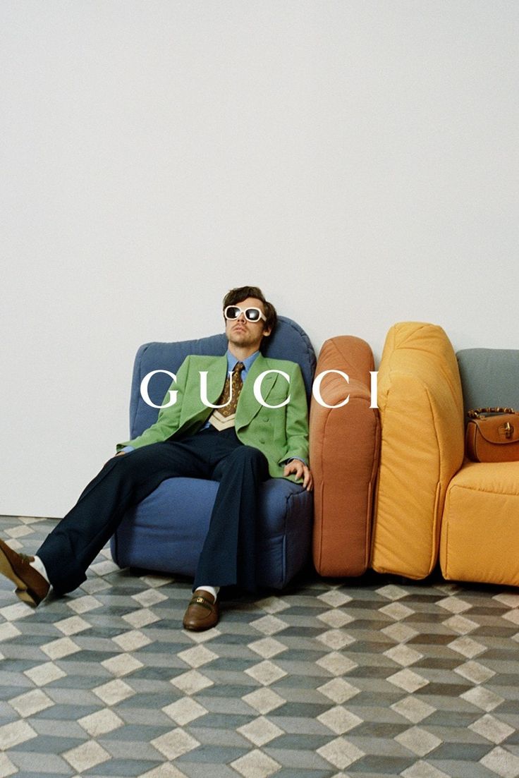 a man sitting on top of a blue couch in front of a wall with the word gucci written across it