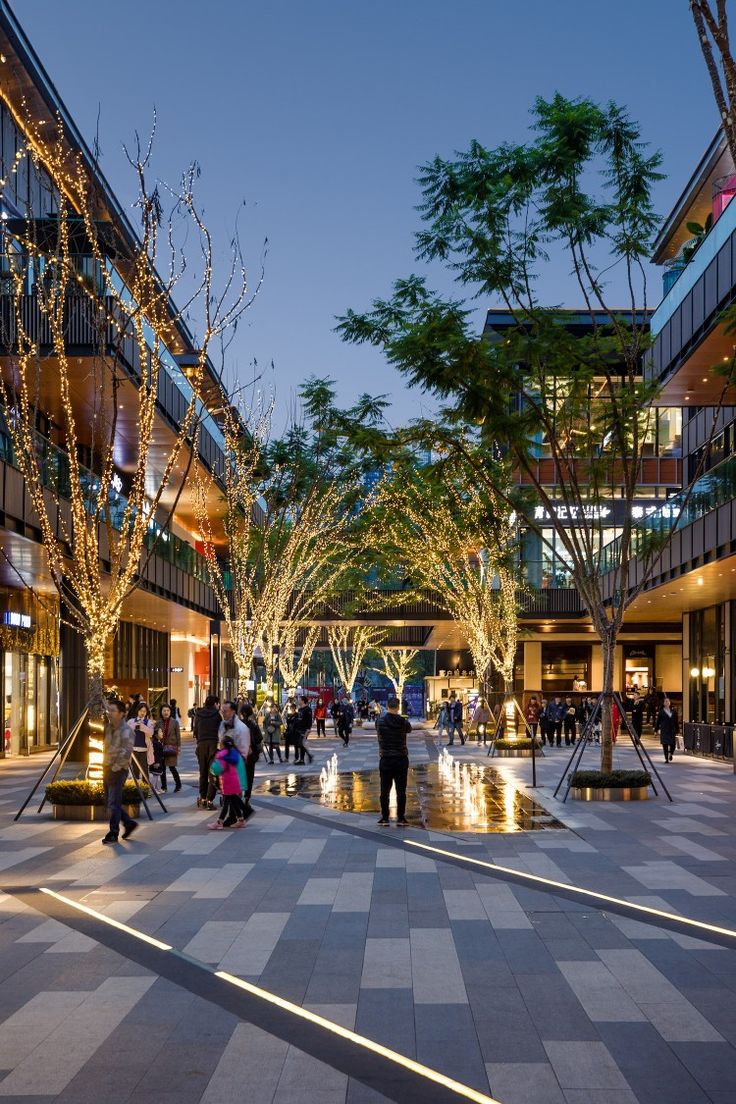 many people are walking around in the city at night with lights on trees and buildings