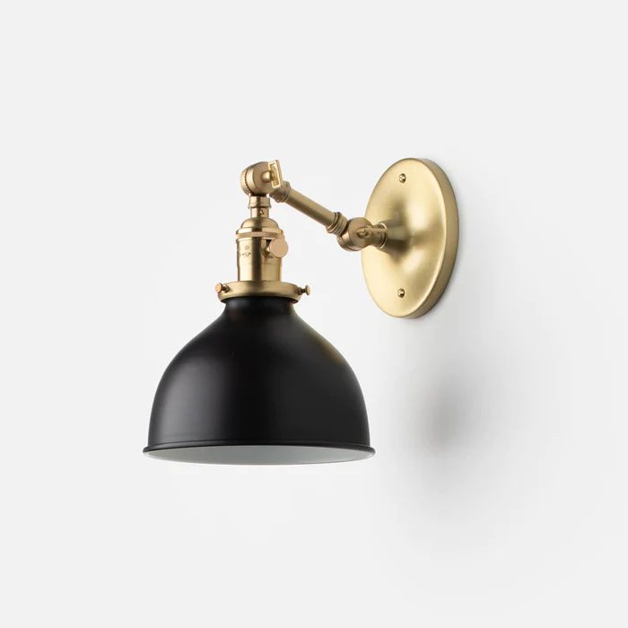 a black and gold wall light against a white background with the arm down to it's head