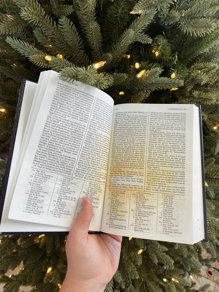 someone is holding an open book in front of a christmas tree