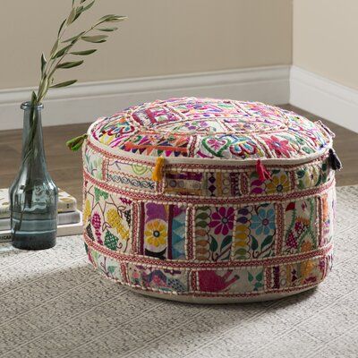 a multicolored patchwork ottoman sits on the floor next to a vase with a flower in it