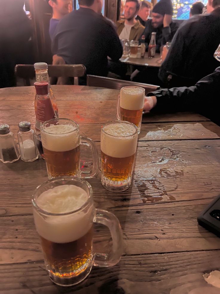 three mugs filled with beer sitting on top of a wooden table