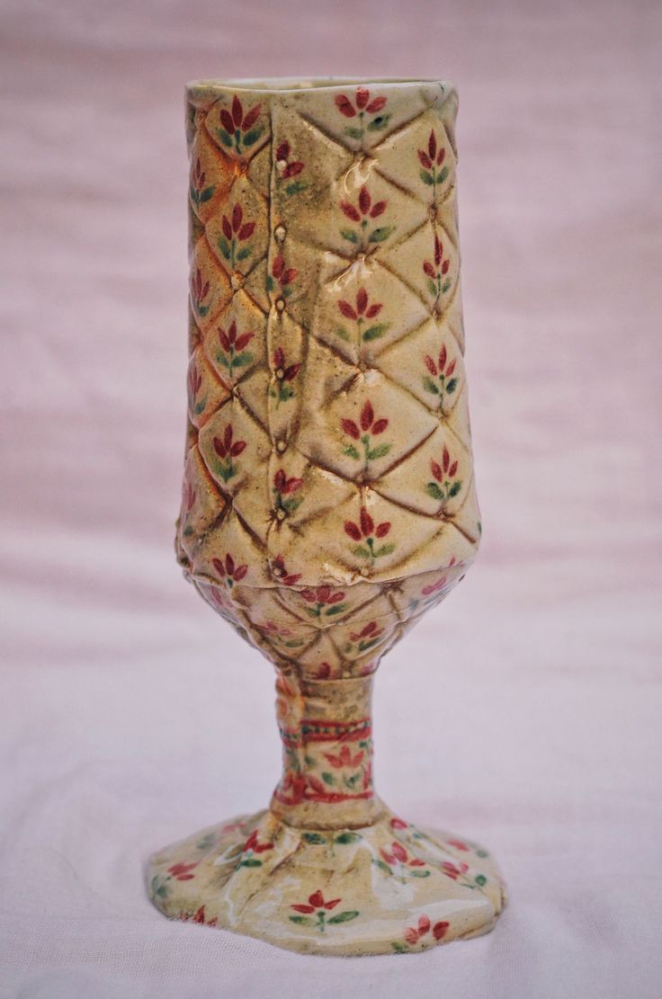 an ornately decorated wine glass on a white tableclothed background with red, green and yellow flowers