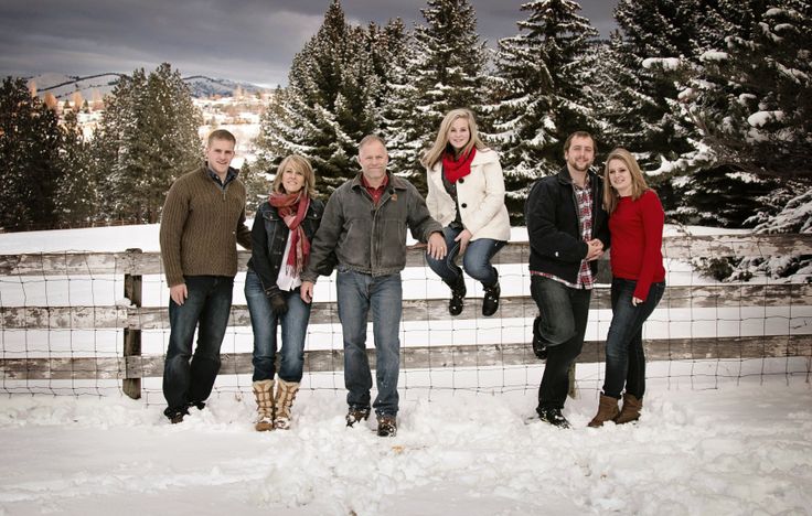 a group of people standing next to each other in front of snow covered trees and fence