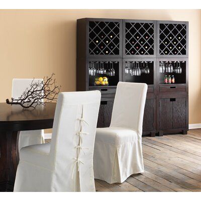 a dining room table with white chairs and a wine rack in the back wall behind it