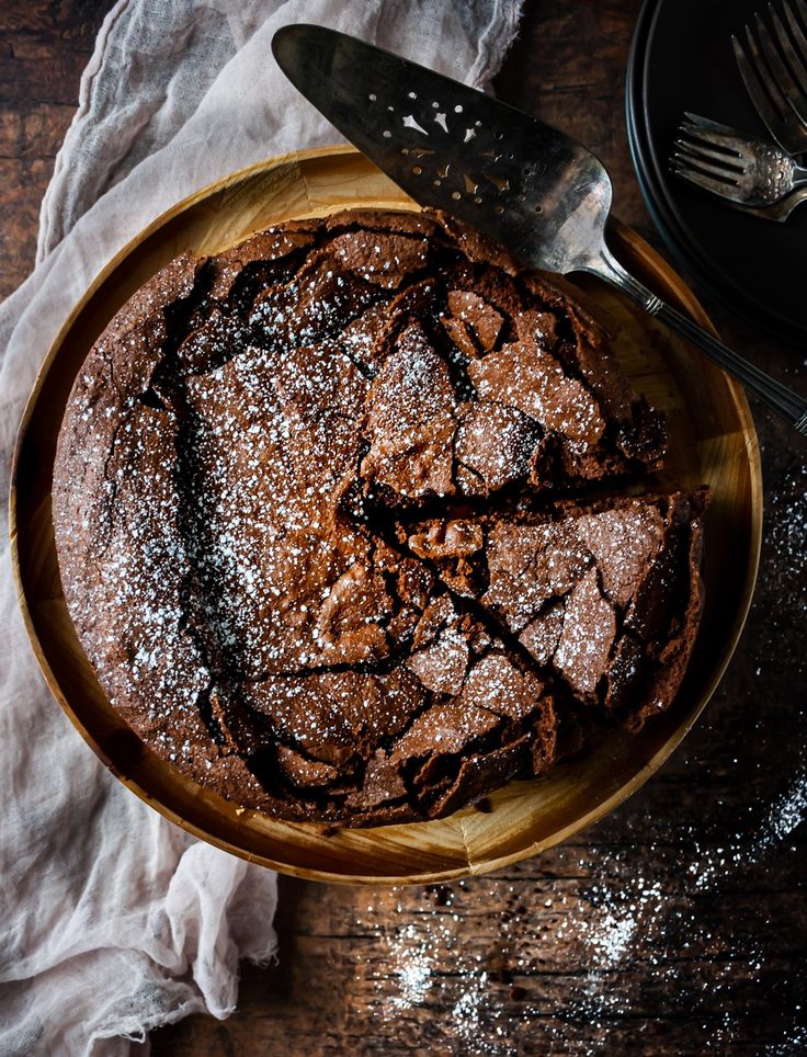 a chocolate cake with powdered sugar on top in a wooden bowl next to a knife