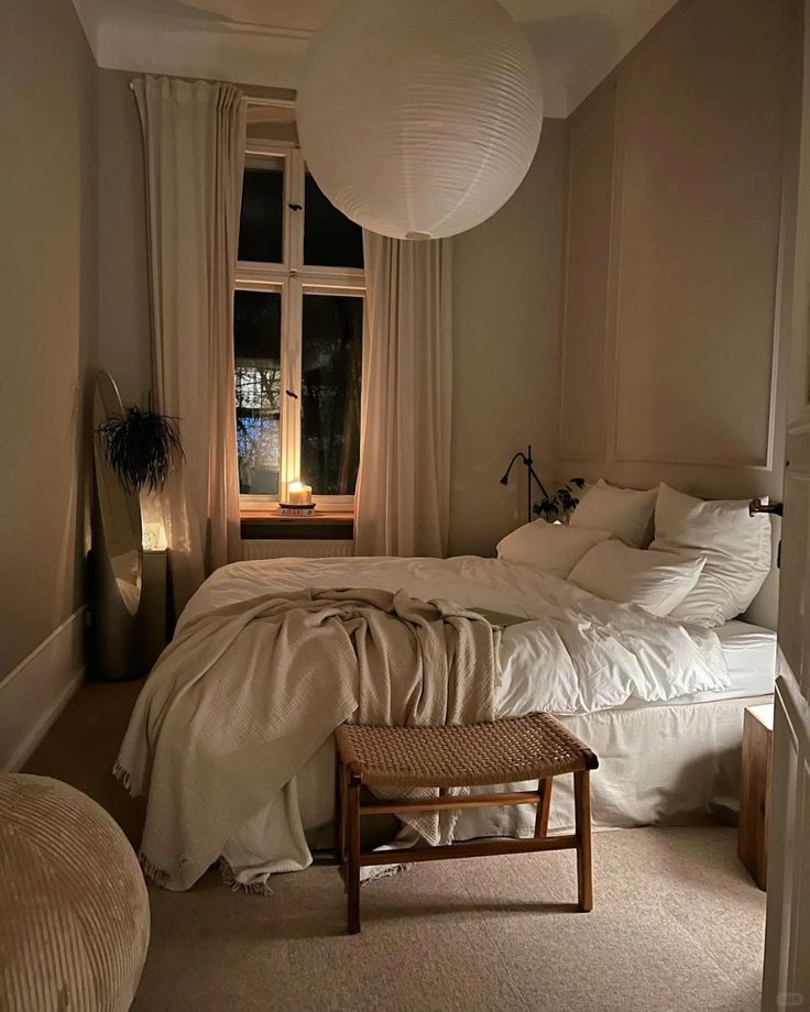 a bedroom with a large bed and white sheets on it's sides, along with a small stool next to the bed