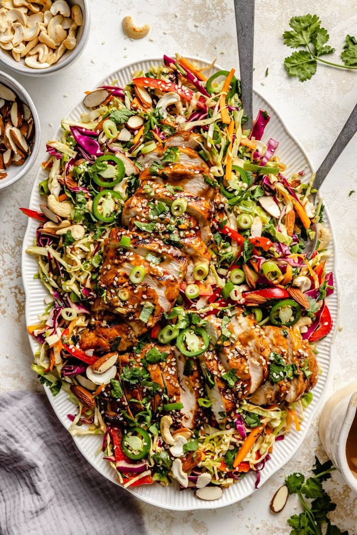 a white plate topped with salad next to bowls of nuts and sauces on a table