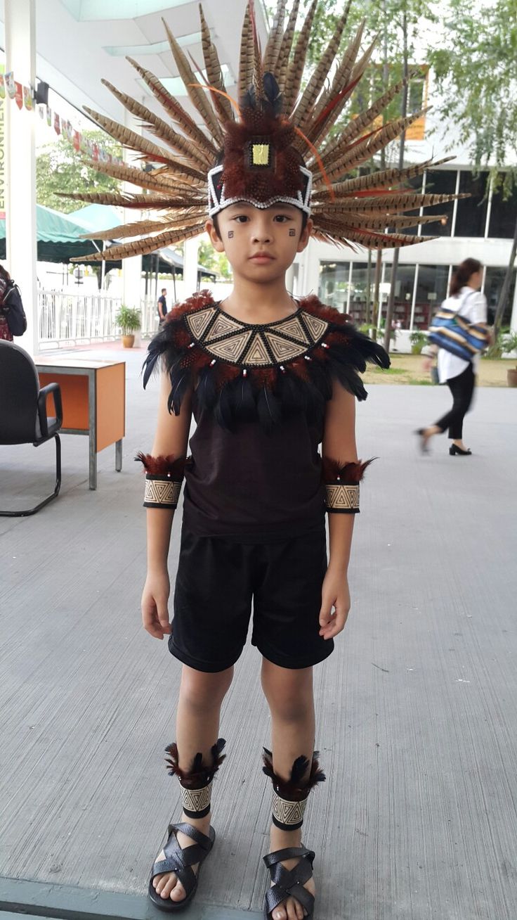 a young boy dressed in native american garb and headdress, standing on the sidewalk