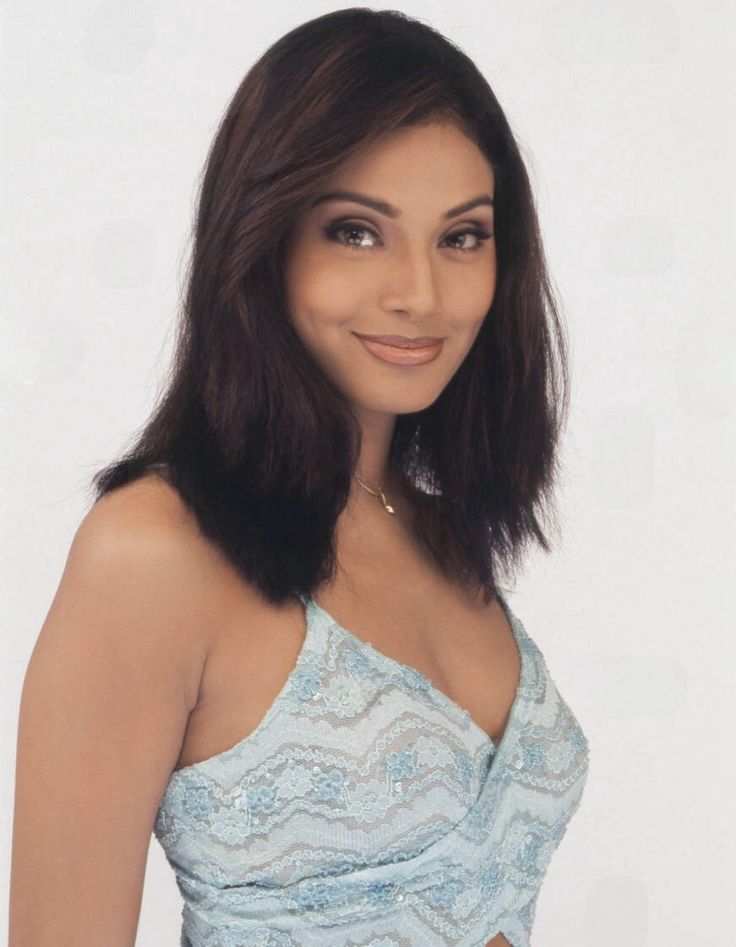 a woman with long dark hair wearing a blue dress and smiling at the camera while standing in front of a white background