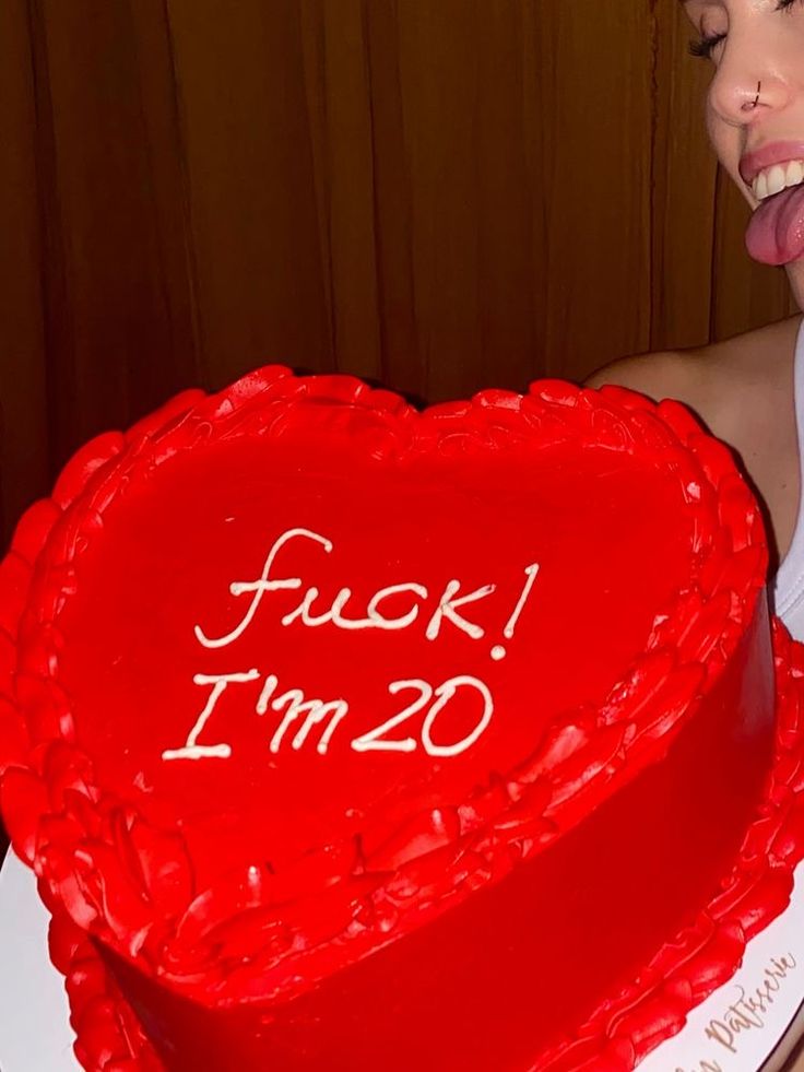 a woman sticking her tongue out in front of a heart shaped cake with the words fock i'm 20 written on it