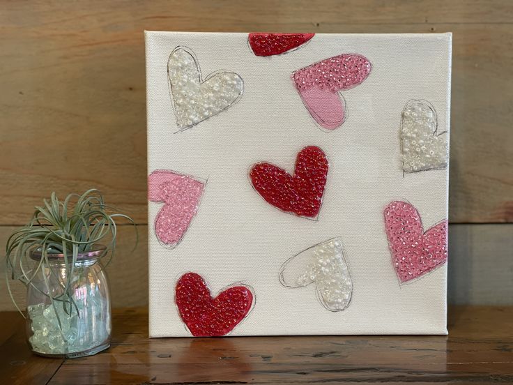 a painting with red, white and pink hearts on it next to a vase filled with air plants