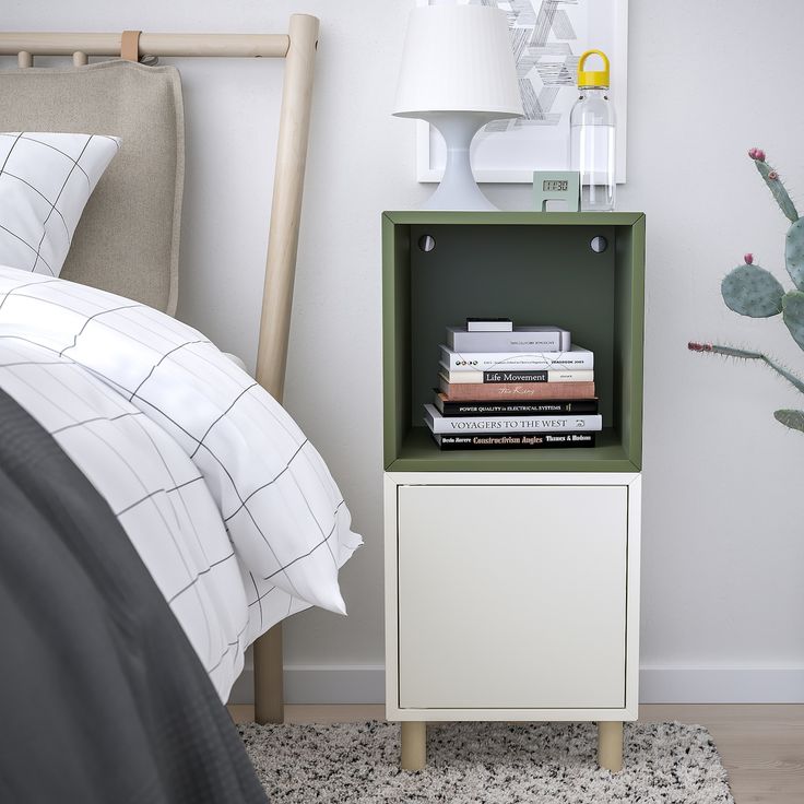 a nightstand with books on top of it next to a bed and cactus in the corner