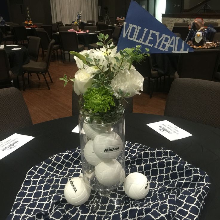 a vase filled with white flowers and balls on top of a blue table cloth covered table