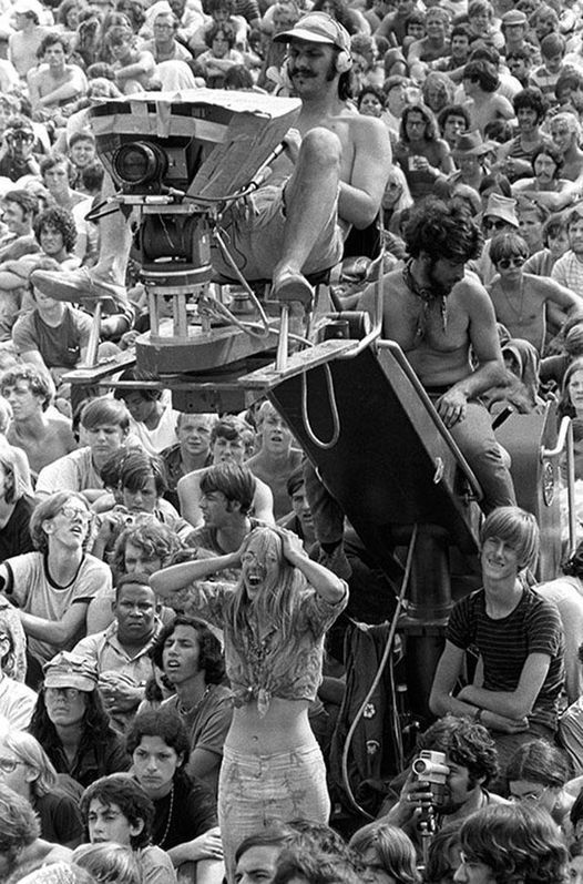 a crowd of people are gathered around a man sitting on top of a chair in front of him