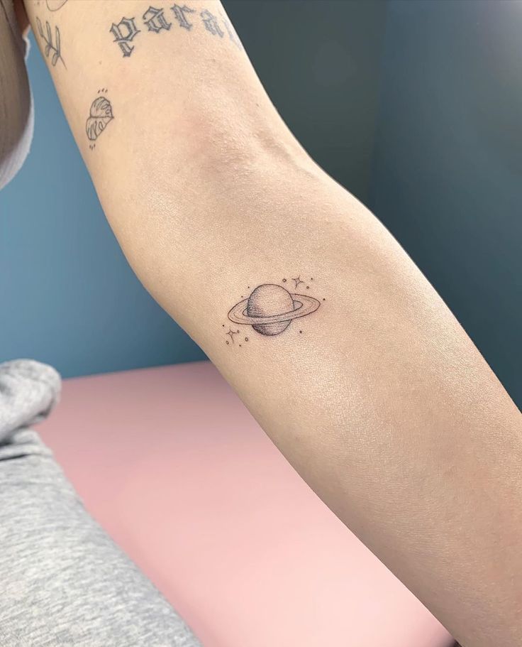 a woman's arm with a small saturn tattoo on the left side of her arm