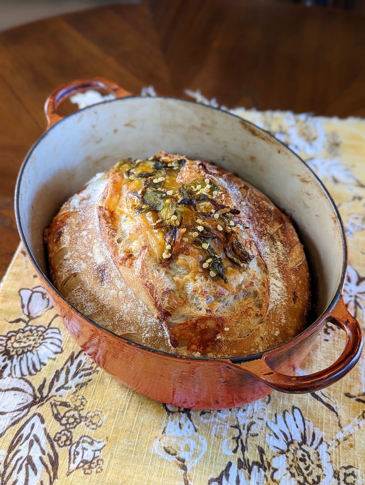 a loaf of bread sitting in a pot on top of a tablecloth covered place mat