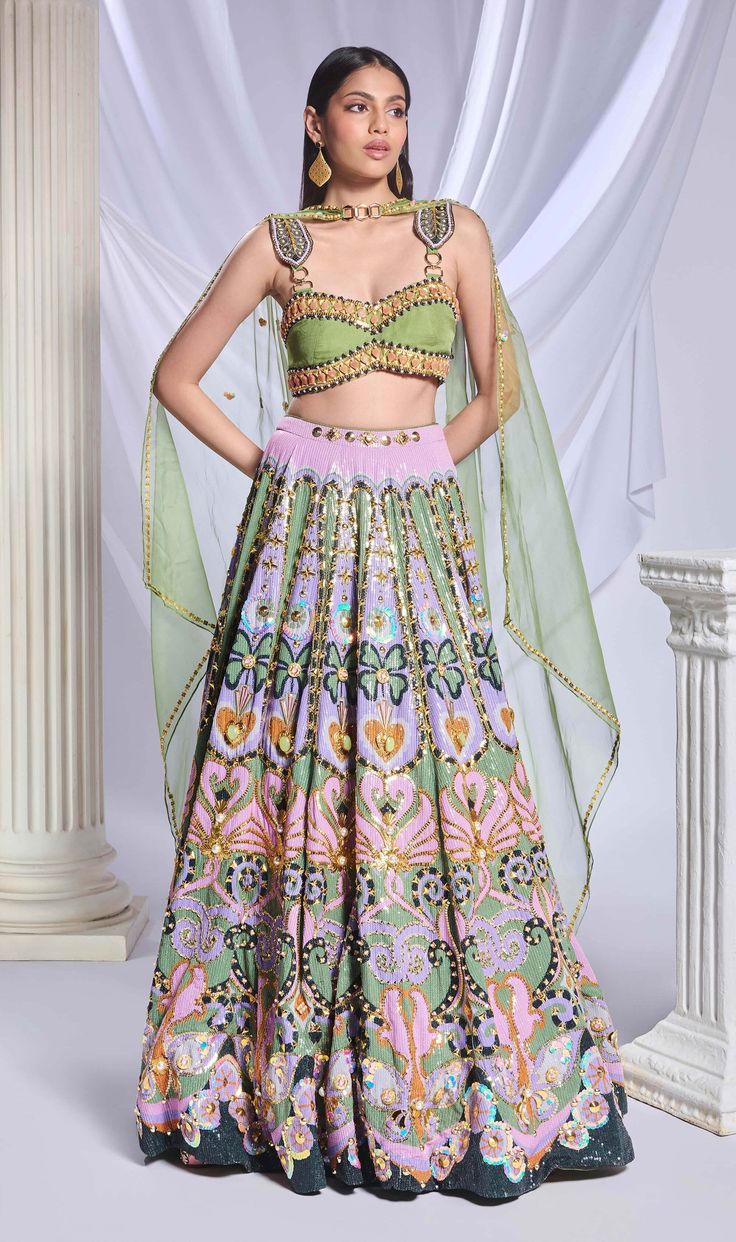 A green sequin-printed lehenga featuring pockets, adorned with gold chains, crystals, pearls and heart-shaped metal accents. It is paired with a green organza blouse, embroidered with gold chains, pearls, glass stones and beads, along with an asymmetrical organza dupatta with a pearl border and sequin scatter. Green Silk Sets For Reception, Anarkali Embellished Green Choli, Anarkali Style Embellished Green Choli, Embellished Green Sharara With Traditional Drape, Green Embellished Anarkali Choli, Bollywood Style Pista Green Sequined Sets, Festive Embellished Green Sharara, Festive Green Embellished Sharara, Bollywood Style Pista Green Sequined Lehenga